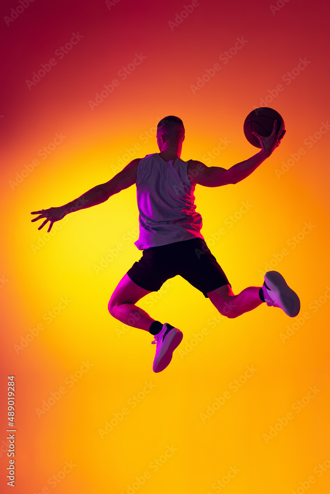 Streetballer. Male basketball player, athlete jumping with ball isolated on gradient yellow orange background in neon light. Sport, diversity, activity concepts.