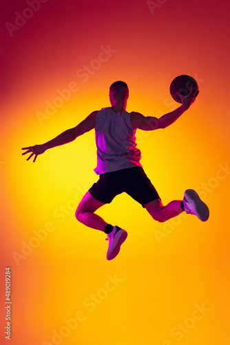 Streetballer. Male basketball player, athlete jumping with ball isolated on gradient yellow orange background in neon light. Sport, diversity, activity concepts. © master1305