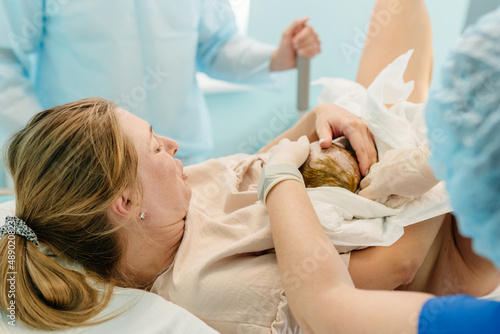 Child birth in maternity hospital. Happy mom with her newborn baby daughter after delivery. Woman giving birth. First moments of baby life after labor.