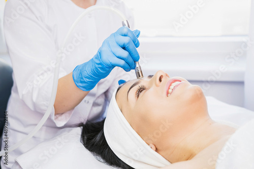 Cropped photo of beautician anhd happy woman lying on the massage table and getting procedure microdermabrasion by a beautician in blue gloves in a cosmetologist clinic.