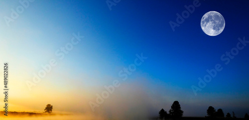 Morning Sunrise with Trees and River Blue Sky and Glowing Mist and Full Moon