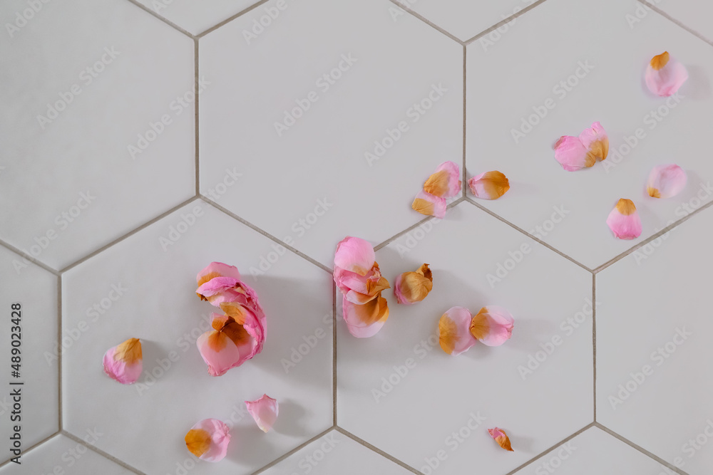Fototapeta premium dry pink rose petal on white tile background with copy space. geometric shape pattern. beauty and wedding decor. holiday card.