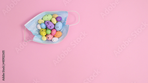 Creative Easter concept with colorful eggs in frace mask on pastel pink background. Flat lay copy space minimal layout © Long Frame