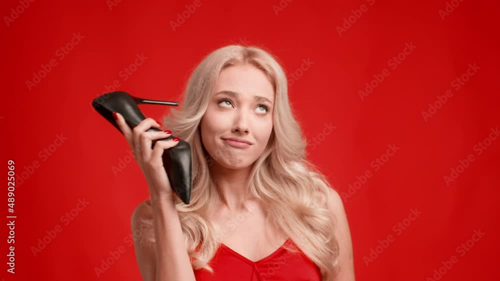 Blonde Woman Talking Holding Shoe Like Cellphone Flirting, Red Background Blonde Woman Talking Holding Shoe Like Cellphone Flirting, Red Background