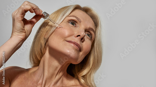 Woman dripping cosmetic oil with dropper on face