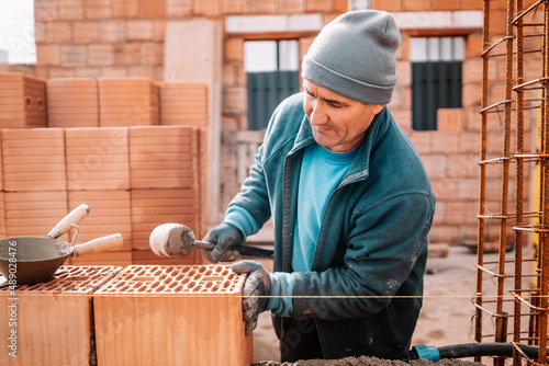 Professional portrait of industrial worker, bricklayer and mason working with bricks and building interior walls of house photo