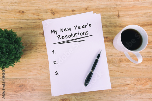 My New Year's Resolutions written on paper with cup of coffee, pen and pot of flower. Retro style wooden background.