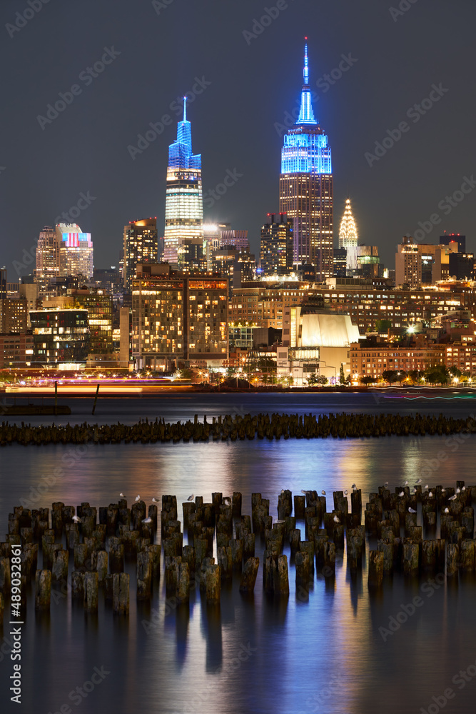 Historic New York skyscrapers illuminated at night from across the Hudson River. Cityscape of West Village and Midtown Manhattan