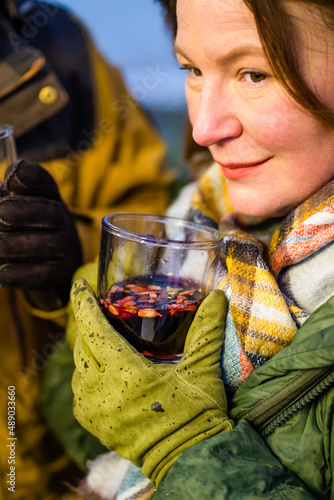 Mature wman enjoying mulled wine sitting near fireplace in romantic tour camping adventure. Romantic mature couple family outreach with hot wine near the fire. Family adventure and vacation concept. 