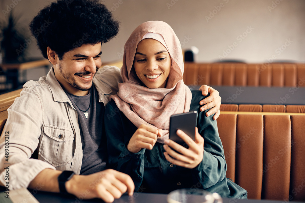 Young happy Muslim couple uses smart phone while relaxing in cafe.