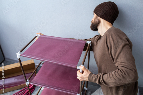 Bearded man assembles a shelf for the rack.