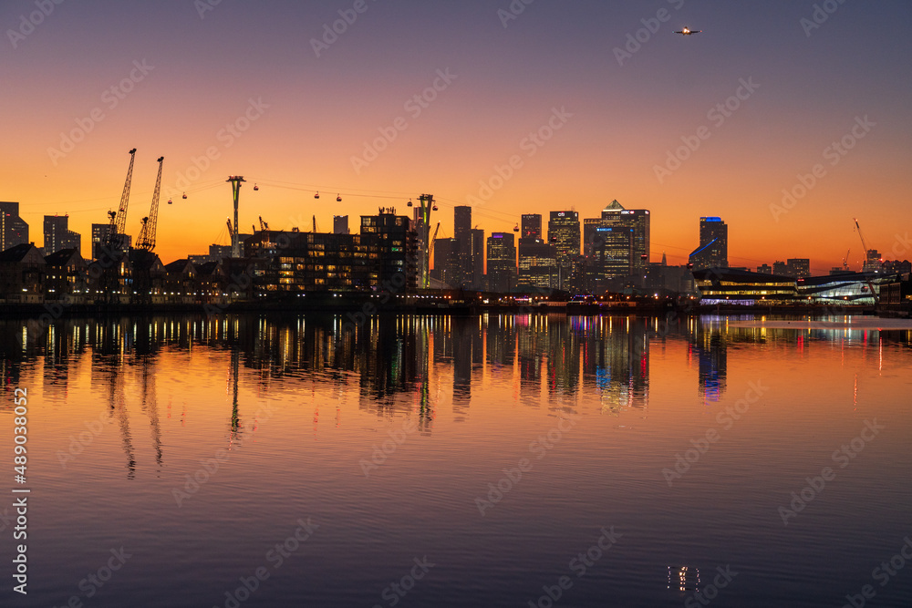 Sunset over the London skyline with orange sky reflecting in the water.