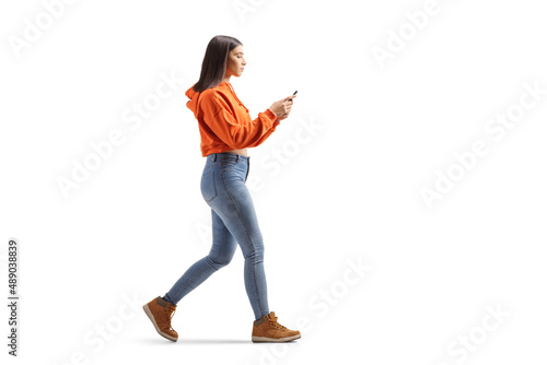 Full length profile shot of a tredny young female walking and using a smartphone