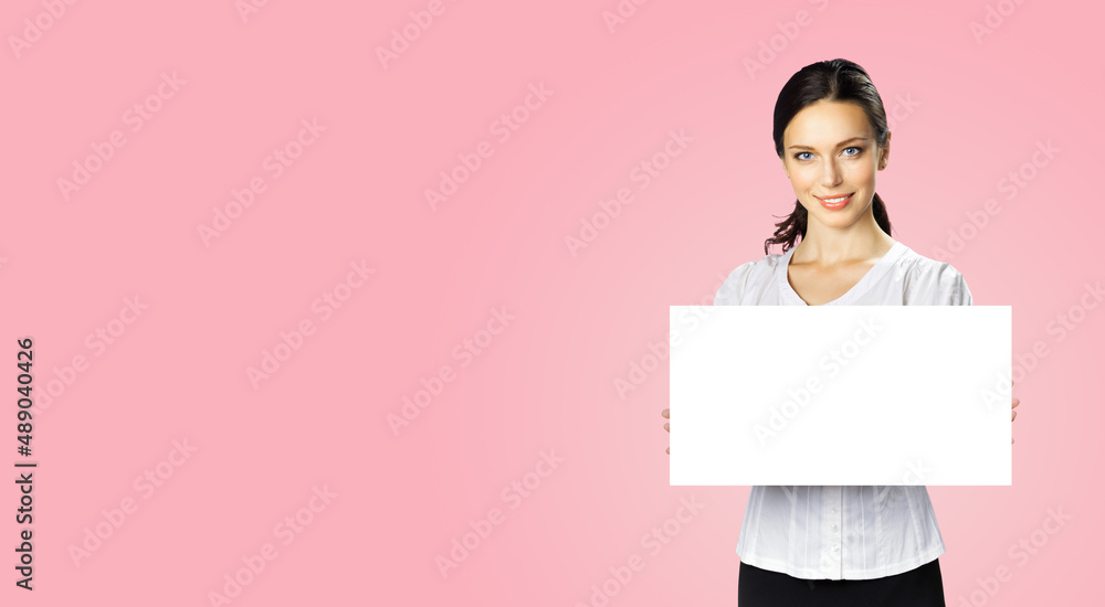 Studio portrait image of happy smiling woman in white confident wear showing blank paper signboard. Business and advertising concept. Copy space empty free area for ad text. Rose pink background. Studio portrait image of happy smiling woman in white confident wear showing blank paper signboard. Business and advertising concept. Copy space empty free area for ad text. Rose pink background.