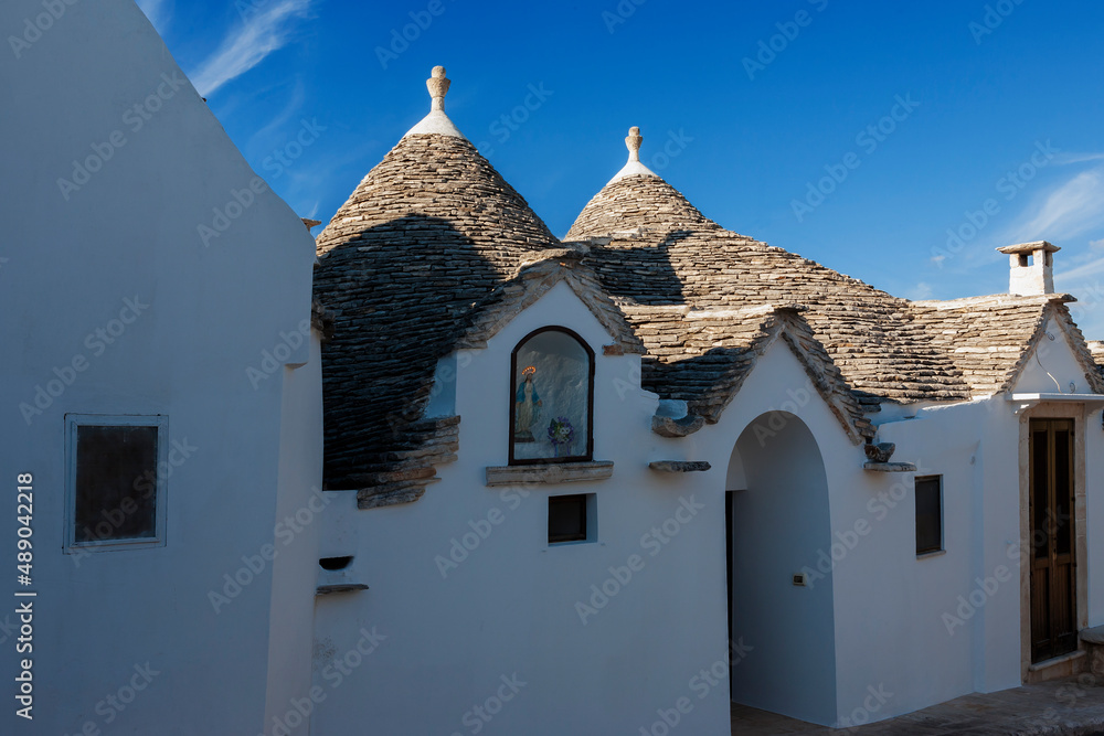 Trulli (traditional dry stone huts with the roof made of dry-set slabs) on Via Giuseppe Verdi, Aia Piccola, Alberobello, Puglia, Southern Italy, with a figure of Christ in a niche in the wall