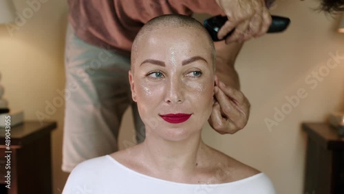 Close-up happy attractive woman is shaved bald with man barber indoor. She is calm and looking at the camera