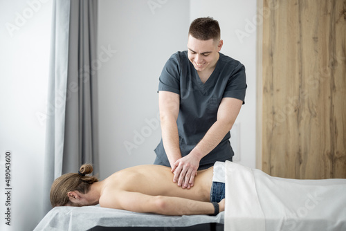 Masseur or manual therapist doing relaxing massage to young man after the training. Concept of relaxing back massage after exercise