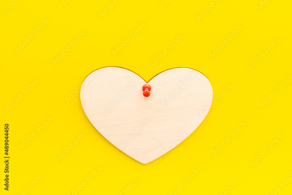 wooden heart on a yellow background pinned with a button