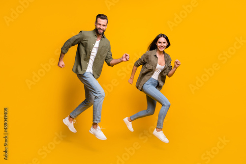 Full length profile side photo of young husband wife fast rush motion runner jumper isolated over yellow color background © deagreez