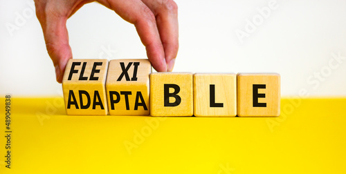 Adaptable or flexible symbol. Businessman turns wooden cubes and changes the word Adaptable to Flexible. Beautiful yellow table white background, copy space. Business, adaptable or flexible concept.