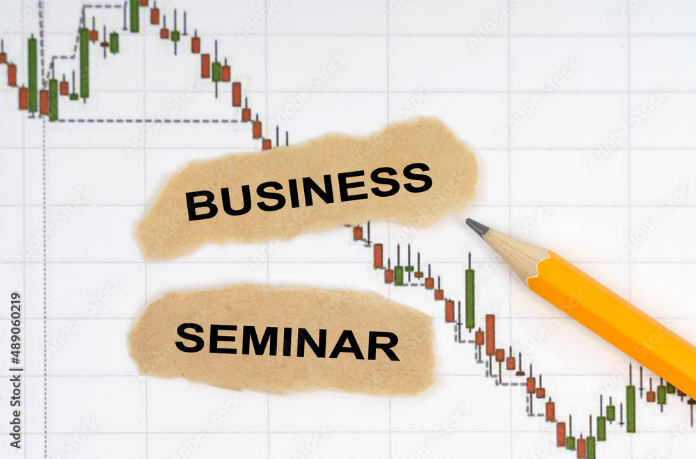 On the table with charts of quotes are a pencil and pieces of paper with the inscription - BUSINESS SEMINAR On the table with charts of quotes are a pencil and pieces of paper with the inscription - BUSINESS SEMINAR