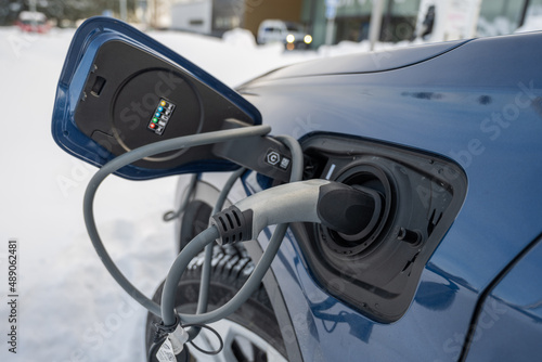 Winter - close up of electric car with a connected charging cable.