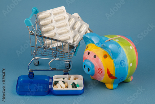 A piggy bank surrounded by pills on a blue background. the medicine. pills. the rise in price of medicines.