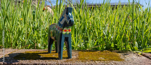 A blue-green wooden Swedish Dala horse outdoors in the sun with a backdrop of tall grass photo