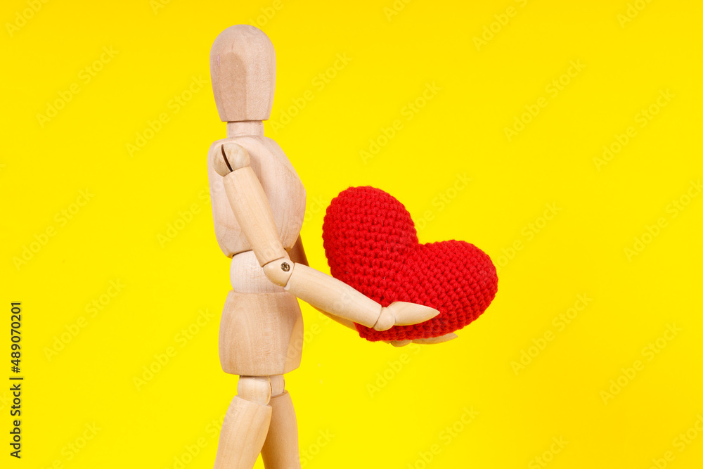 wooden man with a red heart in his hands on a yellow background wooden man with a red heart in his hands on a yellow background