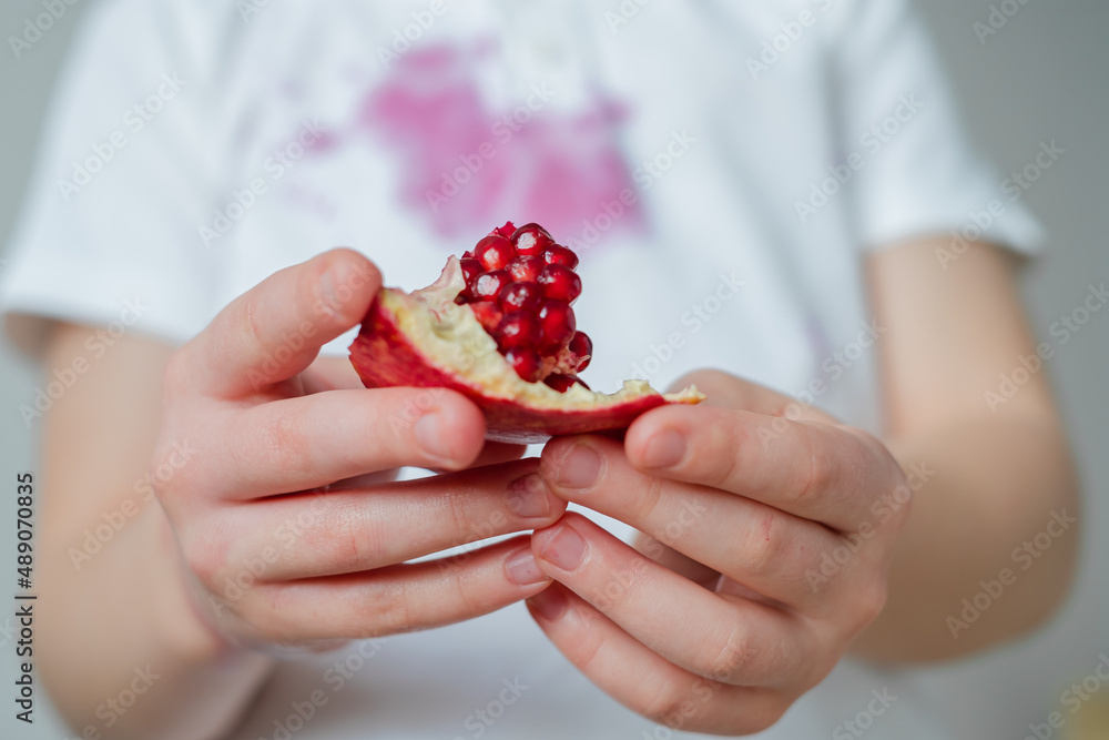 Close up slice of pomegranate seeds in the hands of a child. dirty stain of pomegranate juice after opening on clothes on background Close up slice of pomegranate seeds in the hands of a child. dirty stain of pomegranate juice after opening on clothes on background
