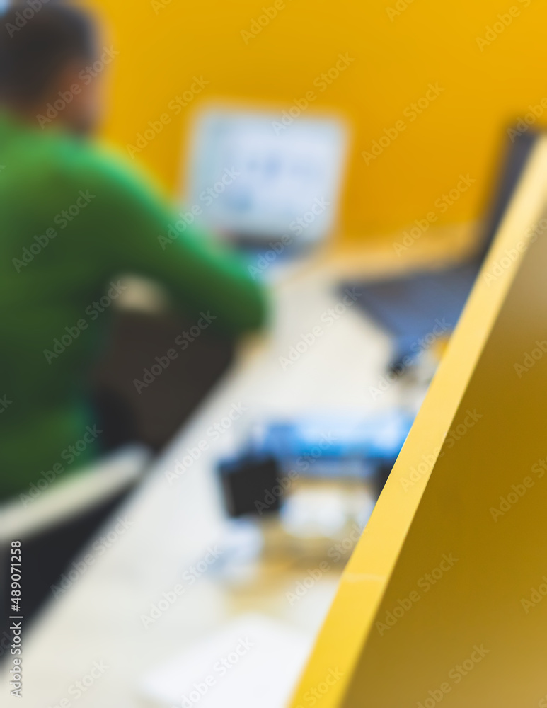 View of modern office space interior with desks in yellow tones with workers, employee with a laptop on a cozy workplace in the background, it-company open space with tables, chairs and rooms View of modern office space interior with desks in yellow tones with workers, employee with a laptop on a cozy workplace in the background, it-company open space with tables, chairs and rooms
