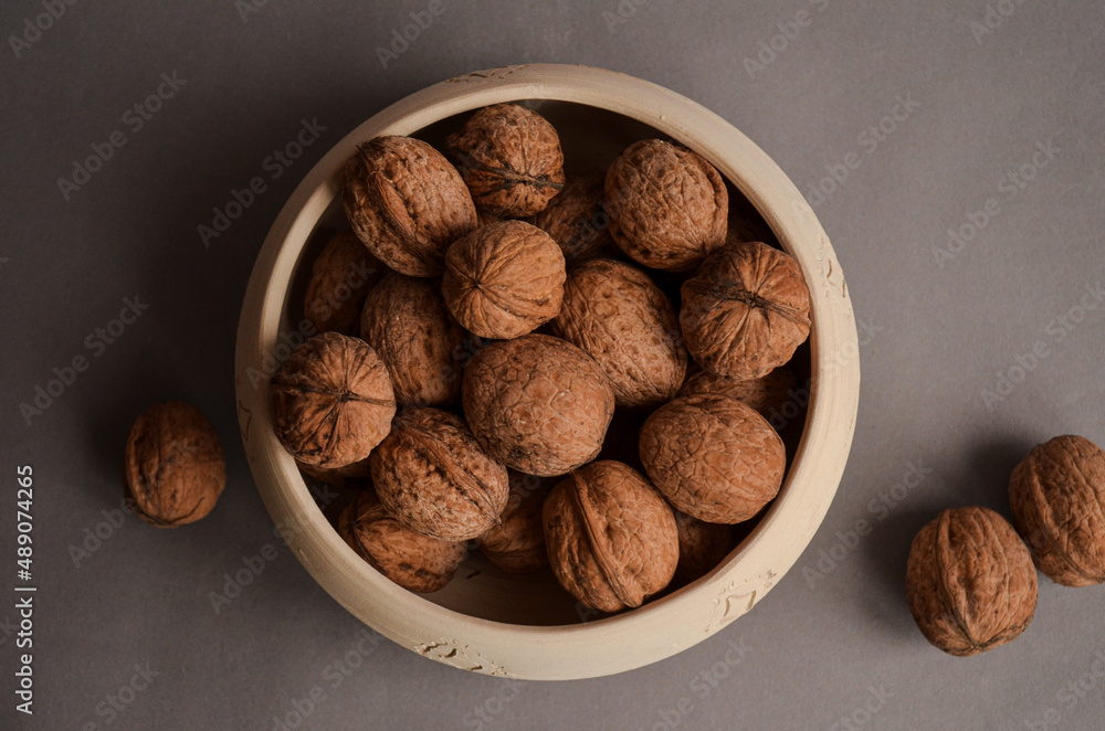 several walnuts lying in a clay bowl and next to it on a gray matte background
