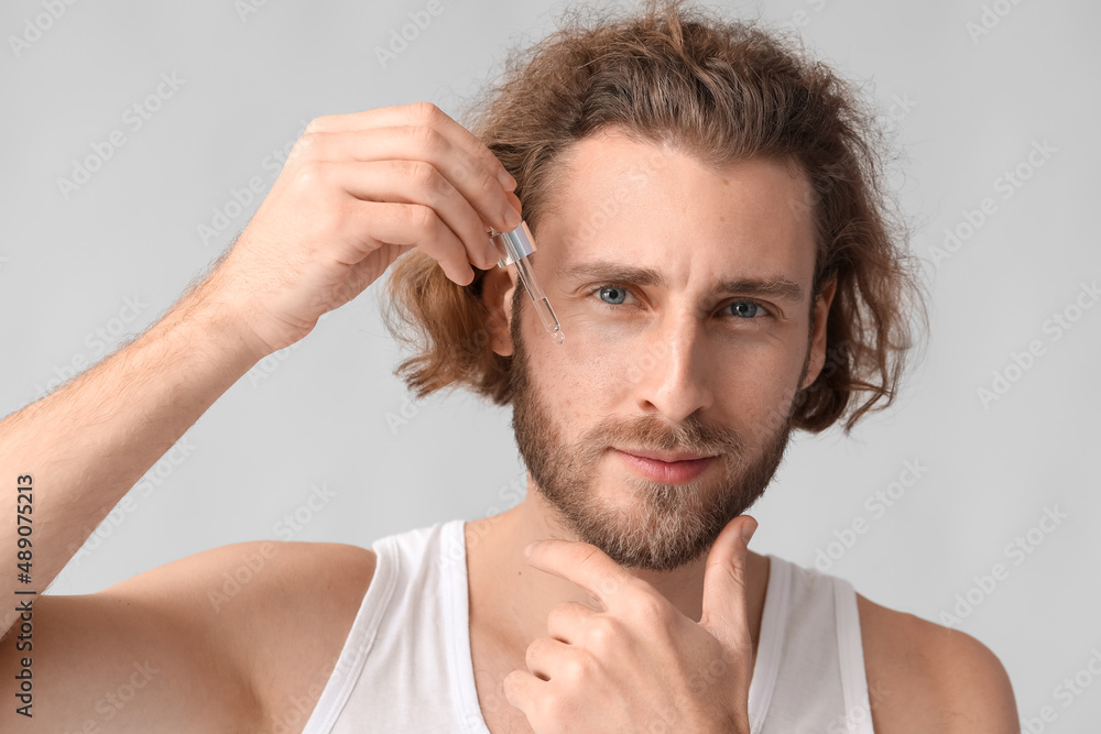 Obraz premium Young man with serum for skin care on grey background