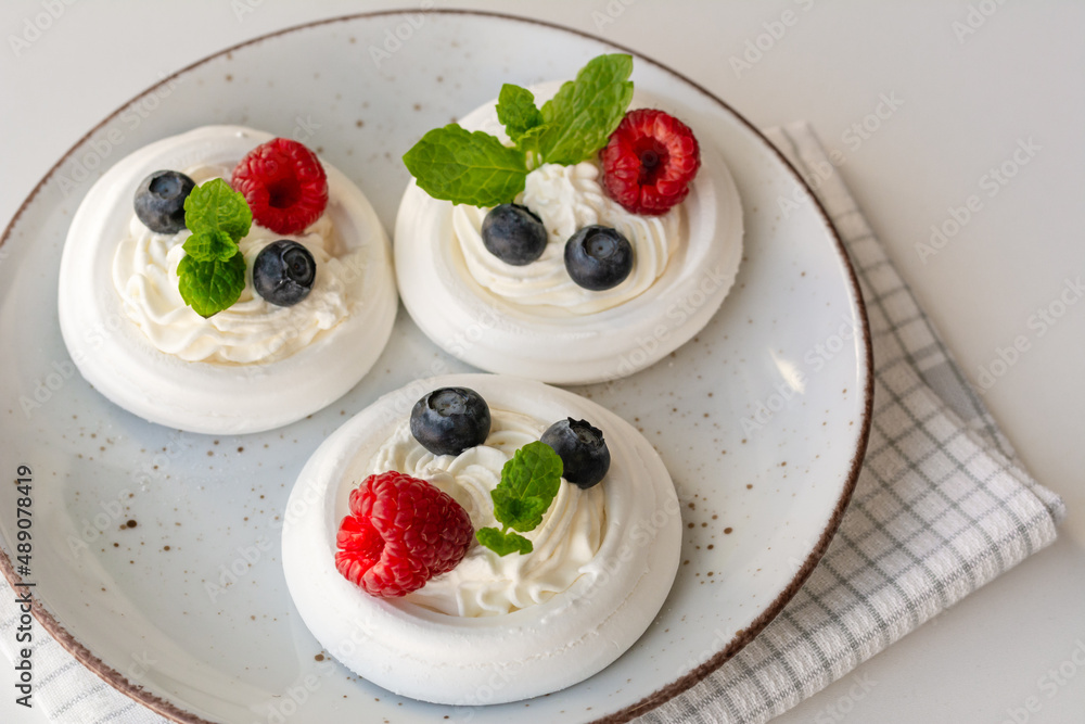 Meringue nests with whipped cream, raspberries, blueberries and a mint leaf Meringue nests with whipped cream, raspberries, blueberries and a mint leaf