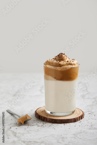 Frappé, cold coffee with milk in a glass on a wood and marble table. Spoon with dulce de leche, salted caramel