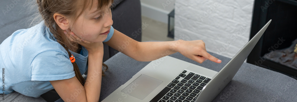 Obraz premium Distance learning. Cheerful little girl girl in headphones using laptop studying through online e-learning system.