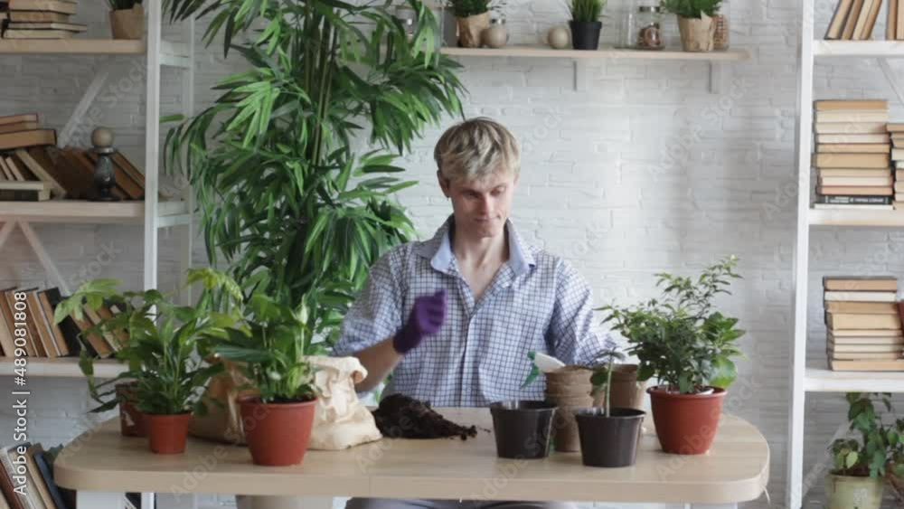 A young guy is sitting at a table putting gloves on his hands going to take care of house plants. Favorite hobby A young guy is sitting at a table putting gloves on his hands going to take care of house plants. Favorite hobby