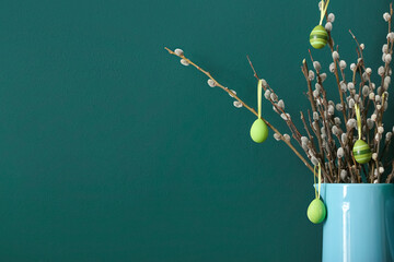 Jug with pussy willow branches and painted Easter eggs on green background, closeup