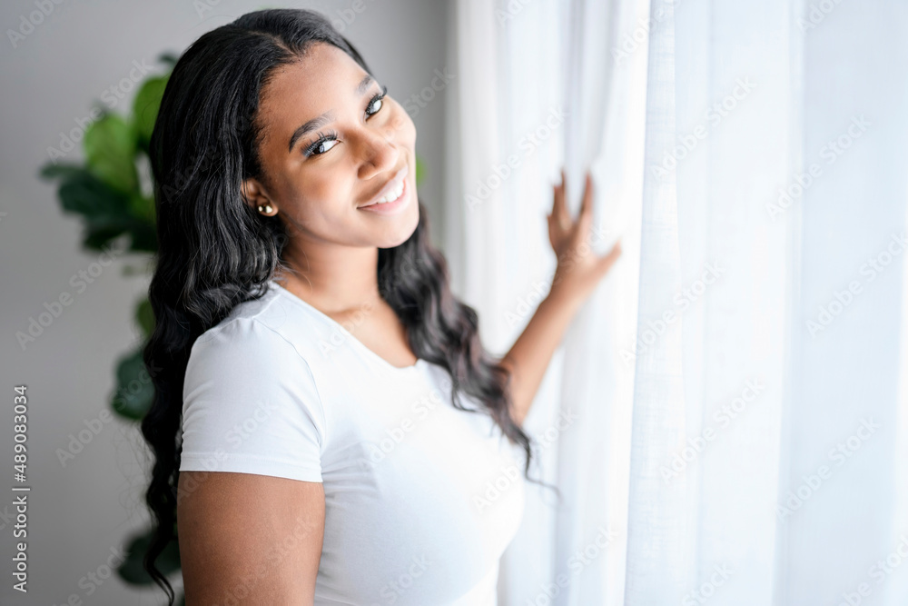 African American woman looking to aside out window, standing at home with smile African American woman looking to aside out window, standing at home with smile