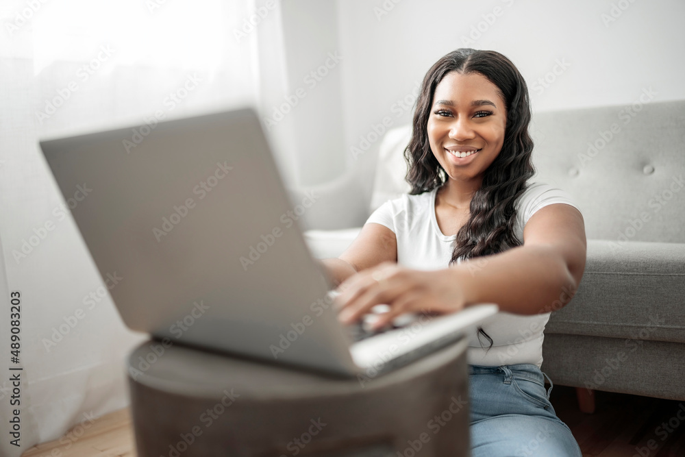 Attractive young African woman working on laptop while sitting on the couch at home Attractive young African woman working on laptop while sitting on the couch at home