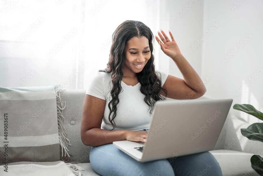 Attractive young African woman working on laptop while sitting on the couch at home say hi Attractive young African woman working on laptop while sitting on the couch at home say hi