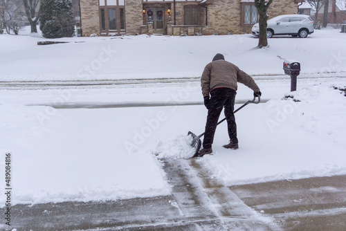 Old man bends over to shovel snow in midwest winter