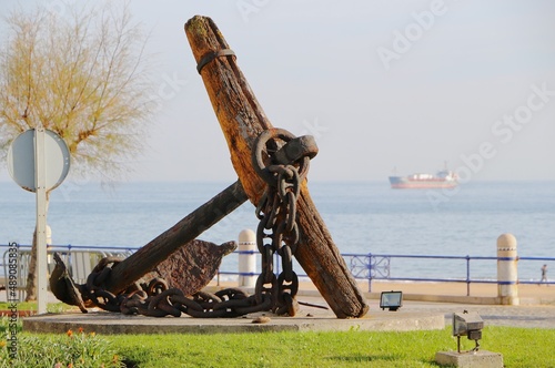 Old weathered wooden and iron ships anchor at a roundabout with an anchored ship in the distance in morning sunshine Santander Cantabria Spain