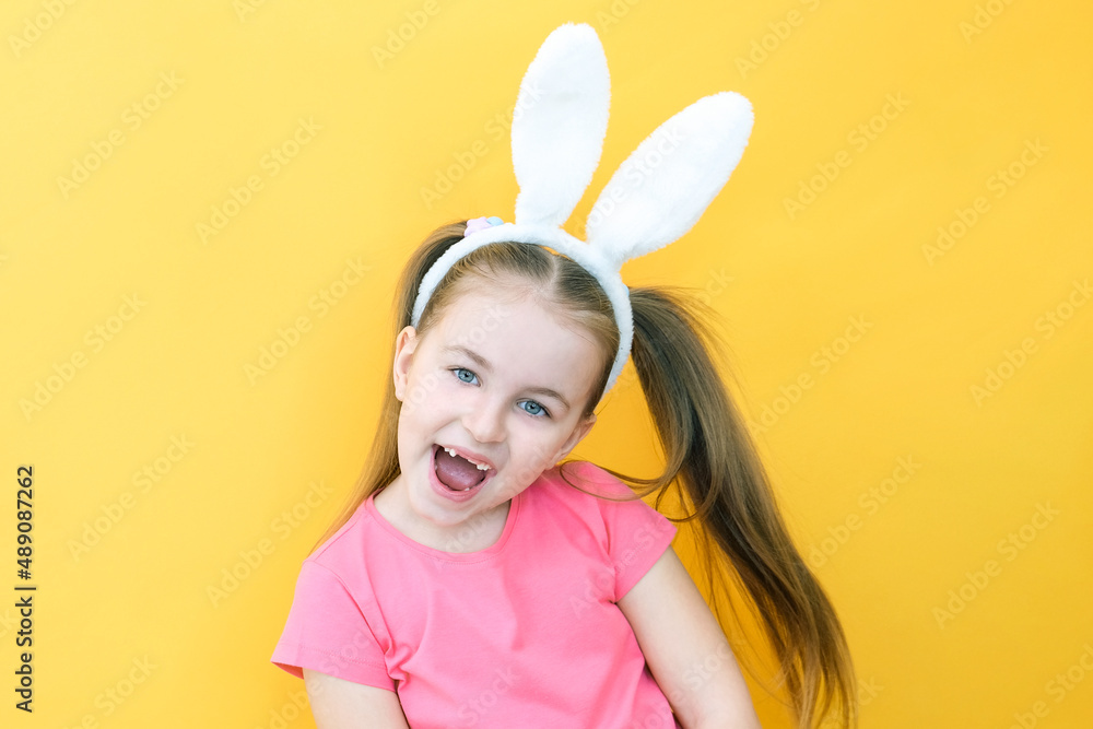 cheerful girl with rabbit ears on her head on a yellow background. Funny crazy happy child. Easter child. Preparation for the Easter holiday. promotional items. copy space for text