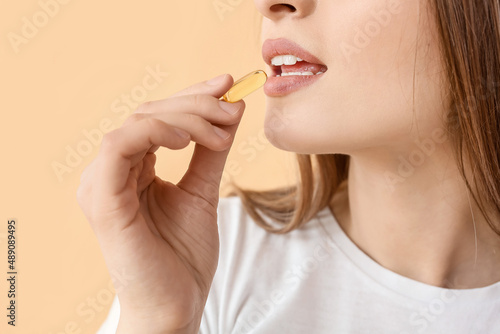 Young woman with healthy fish oil pill on color background  closeup