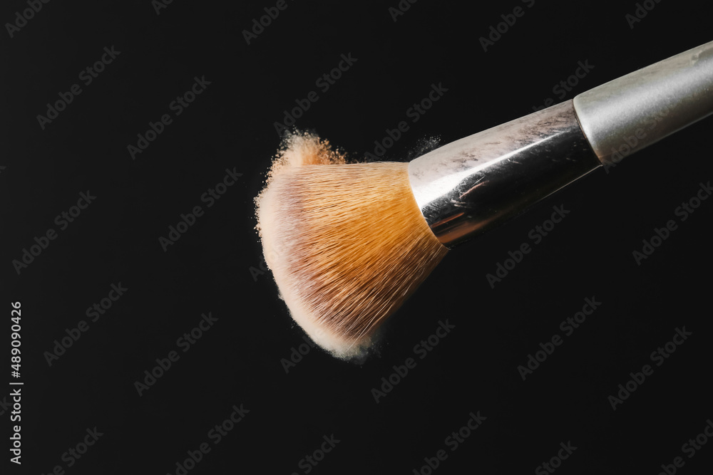 Fototapeta premium Makeup brush shaking off powder on black background