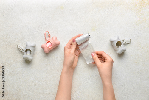 Female hands with pet waste bags and dispensers on light background