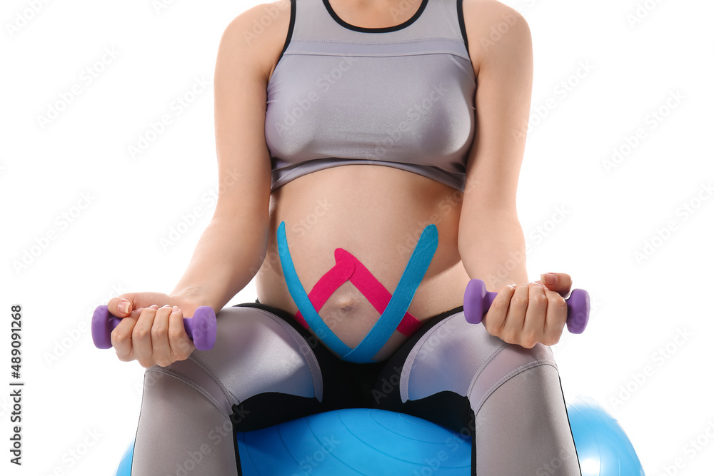 Fototapeta premium Pregnant woman with applied kinesio tape training against white background