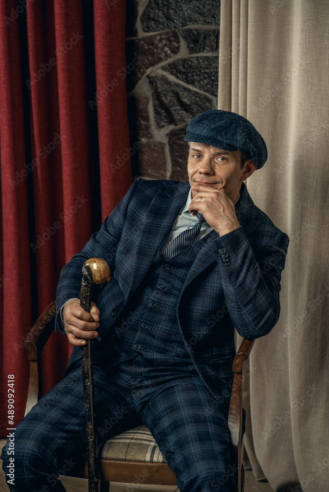 A man posing in the image of an English retro gangster of the 1920s dressed  in a suit and flat cap in Peaky blinders style Stock Photo | Adobe Stock