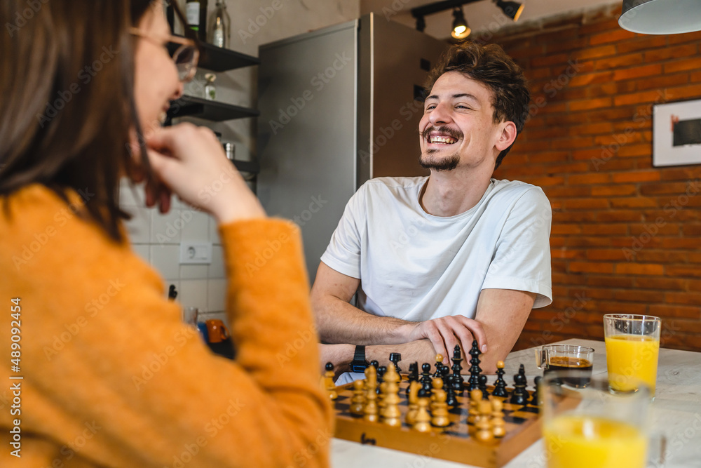 young couple playing chess while sitting at table at home - Unpacked